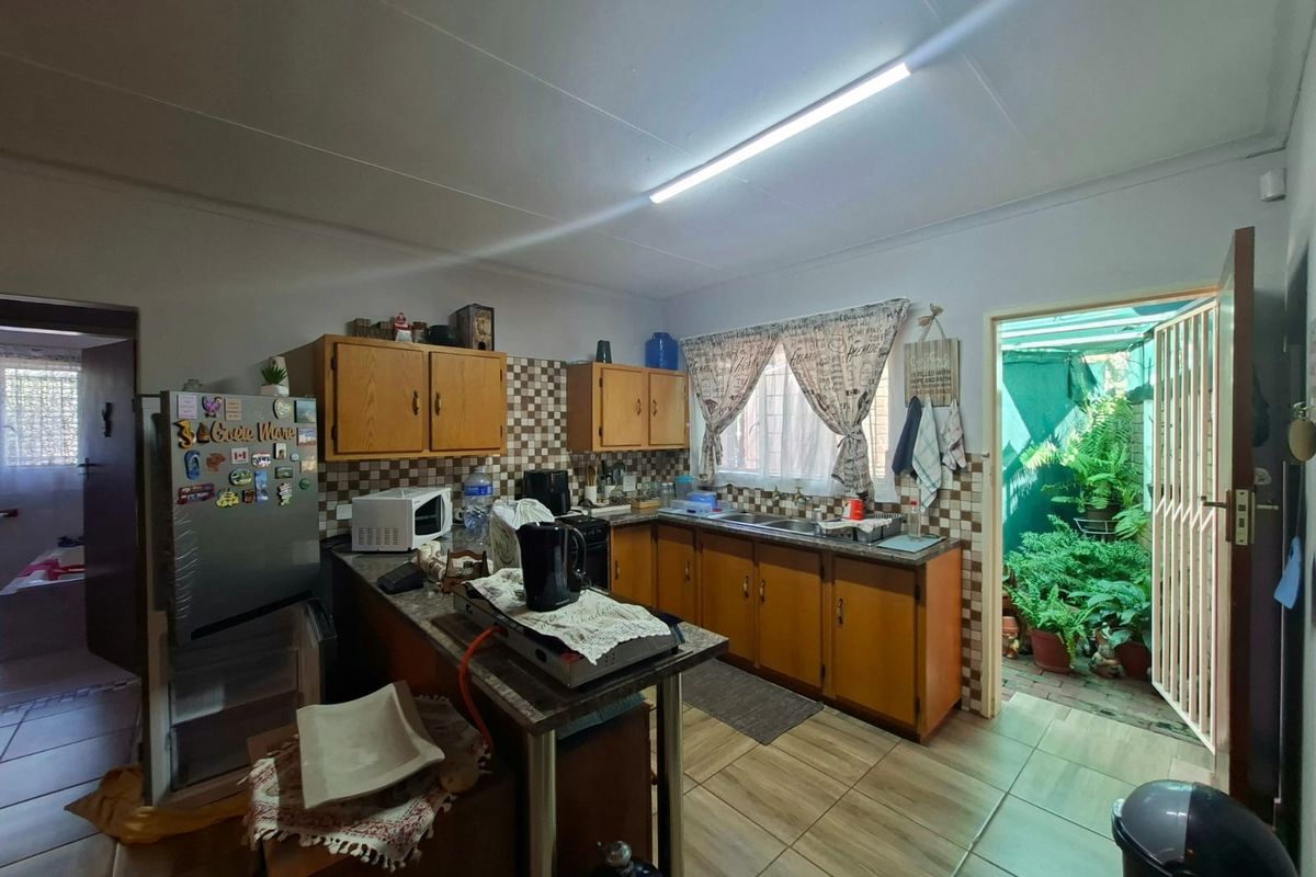 A functional kitchen featuring wooden cabinetry, tiled backsplash, and direct access to an outdoor area through a security gate.