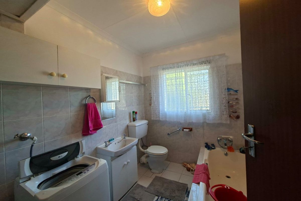 A functional bathroom featuring a bathtub, toilet, vanity basin, and wall tiling, with space for laundry appliances.