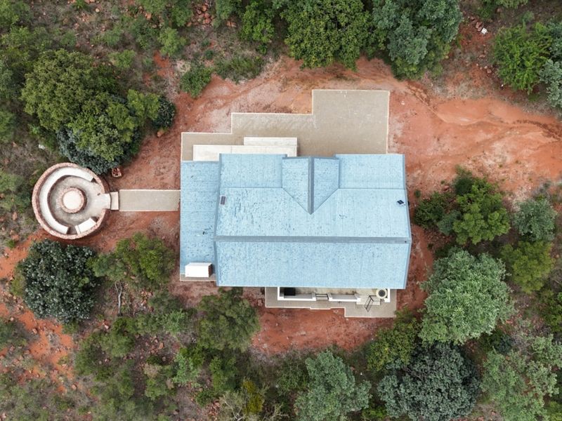 Aerial view of a residential property featuring a metal roof, paved patio area, and a circular outdoor fire pit set within a natural landscape.