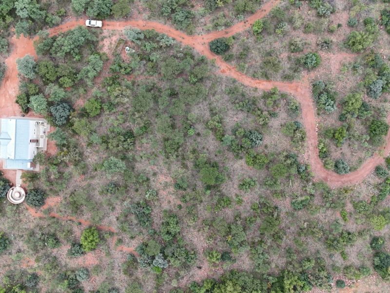 Aerial view of a secluded property featuring a main dwelling with a metal roof, a circular patio, and a winding dirt access road.