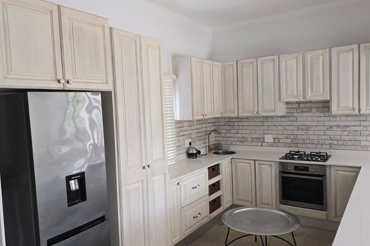 A well-maintained kitchen featuring light-toned cabinetry, stone countertops, a brick-style backsplash, and integrated stainless steel appliances.