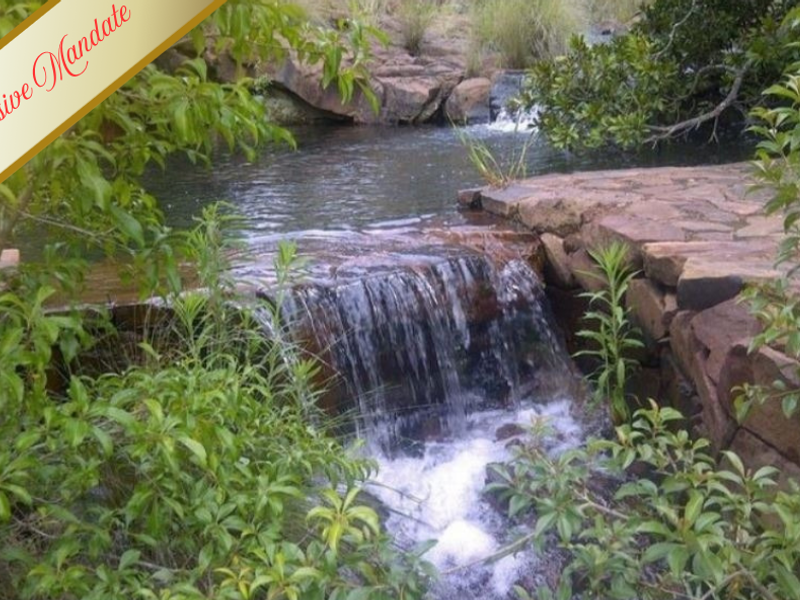 A scenic view of a natural stream featuring a small waterfall and stone retaining wall, highlighting the property's natural landscape features.