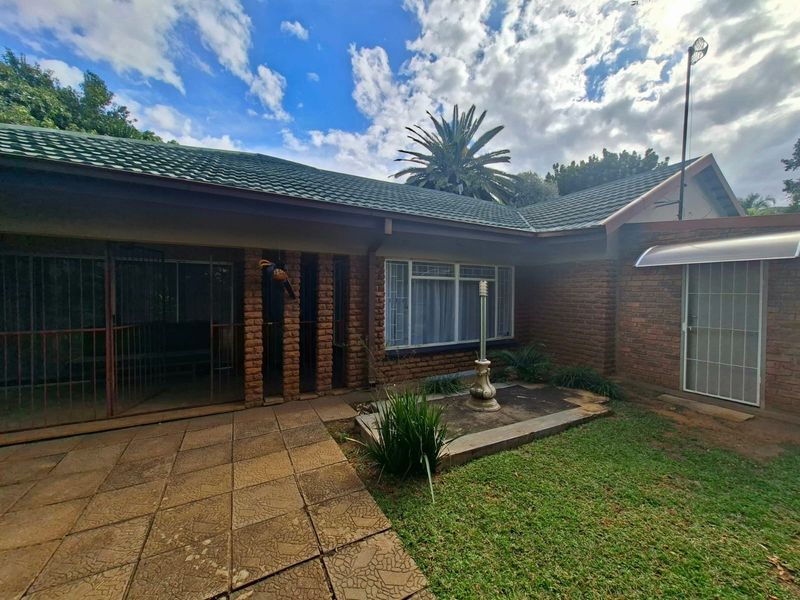Rear exterior view of the house featuring a brick facade, tiled roof, paved patio area, and a small garden space.