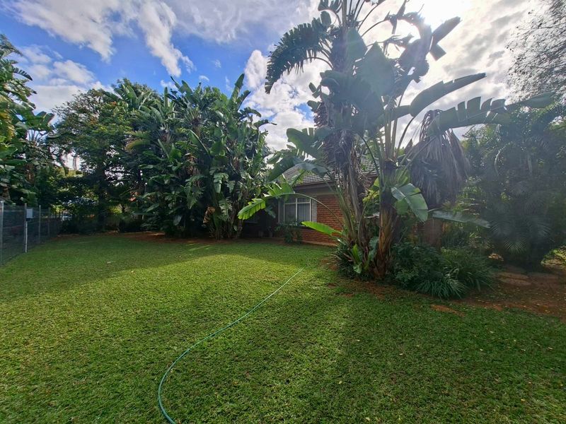 A spacious private garden featuring a well-maintained lawn, mature landscaping, and a brick exterior wall of the house.
