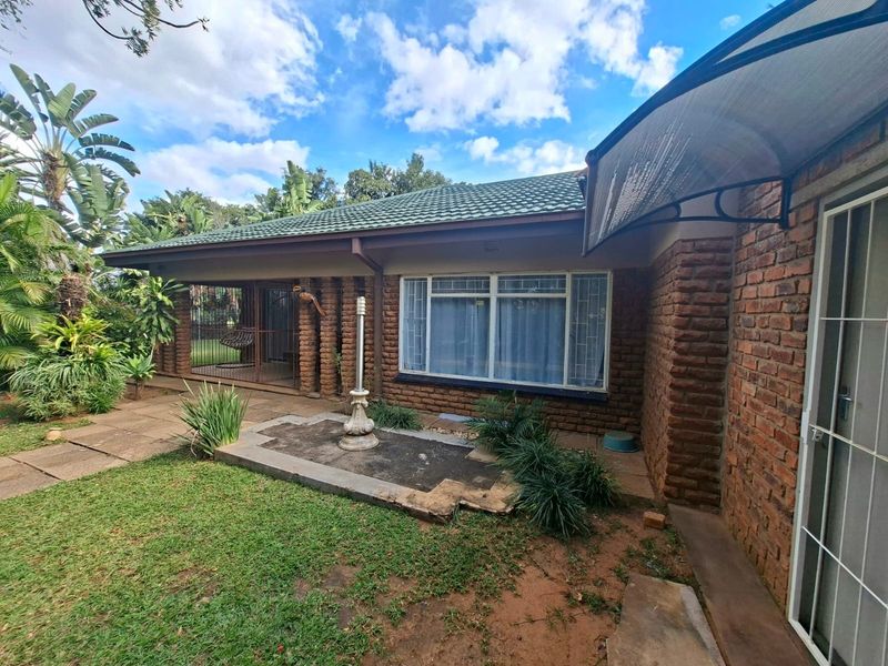 Rear view of the house featuring a face brick facade, tiled roof, and a covered patio area with paved garden access.