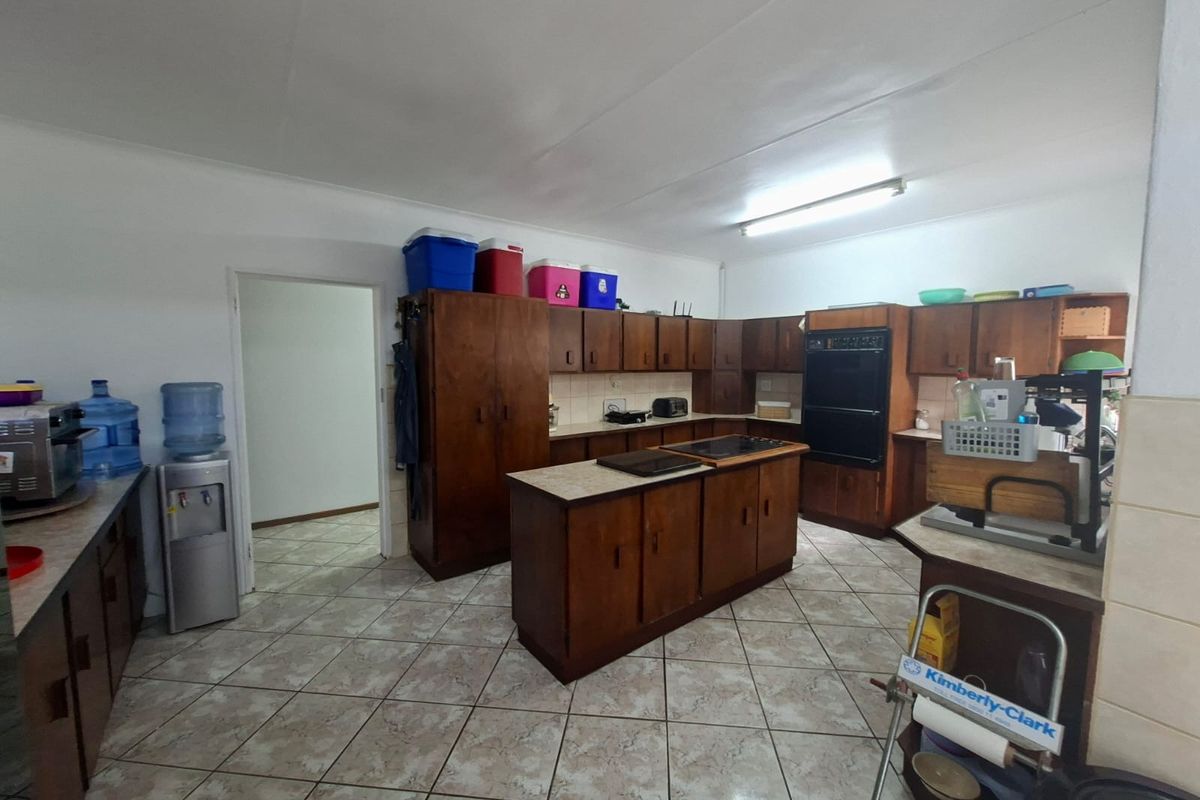 A spacious kitchen featuring extensive wooden cabinetry, a central island, built-in oven, and tiled flooring, offering significant potential for modernization.