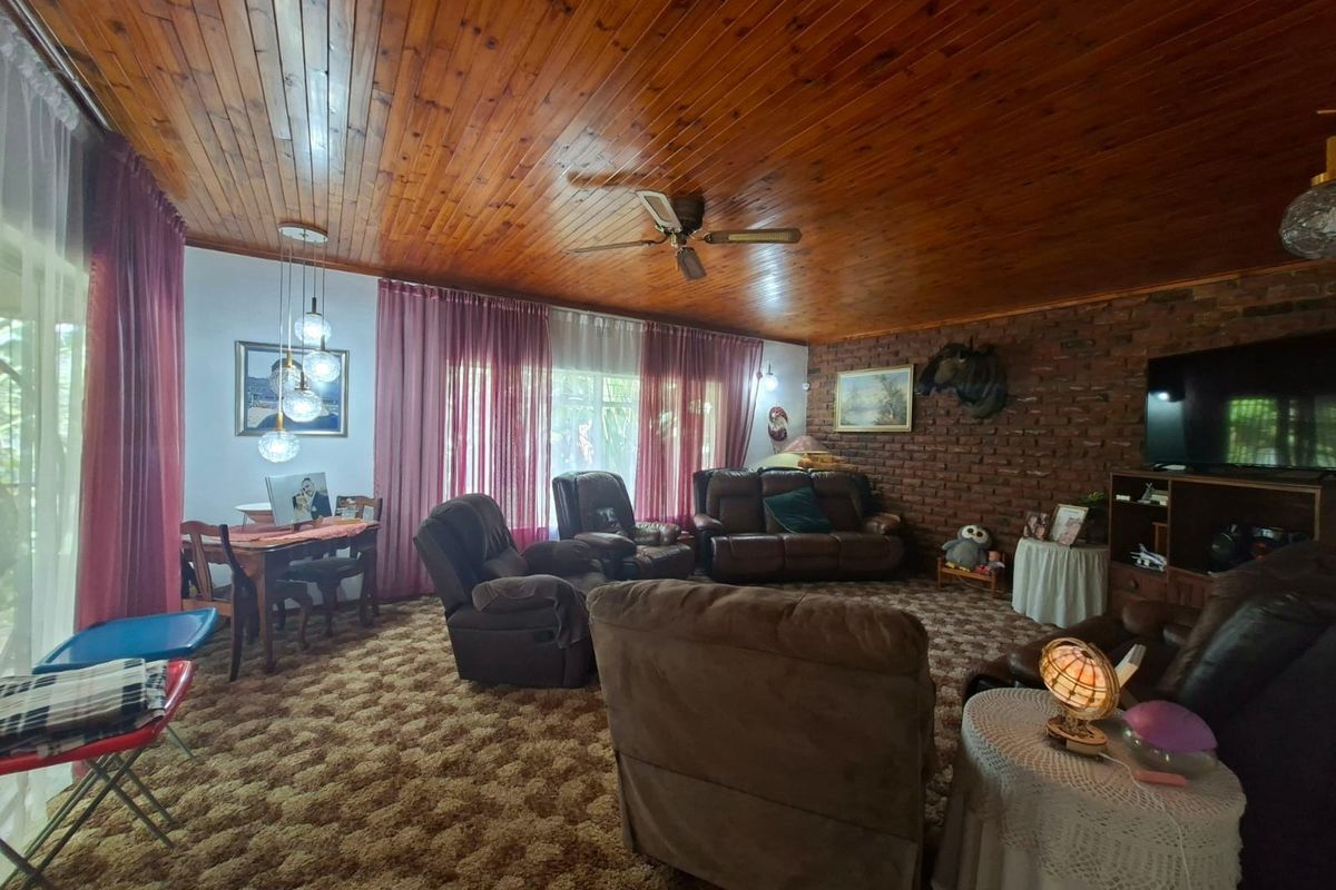 Spacious living room featuring a warm timber-clad ceiling, an exposed brick feature wall, and a ceiling fan, offering a cozy and traditional atmosphere.
