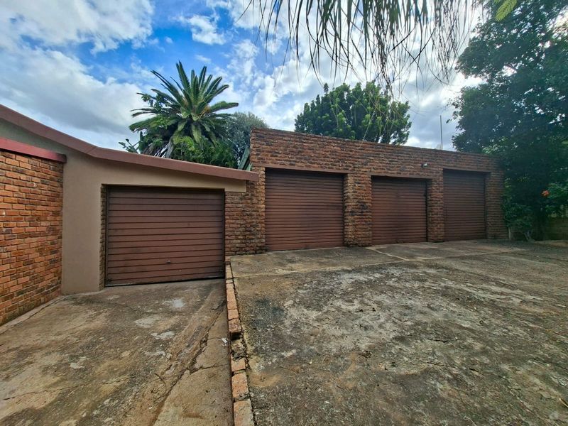 A four-car garage featuring brick exterior walls and a concrete driveway, showing signs of age and weathering.