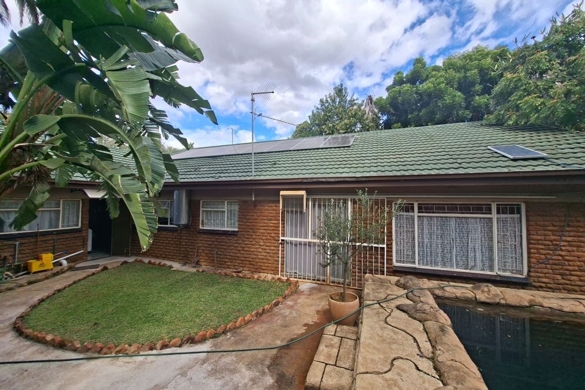 Rear exterior view of the house featuring a brick facade, tiled roof with solar panels, and a swimming pool area with adjacent garden space.