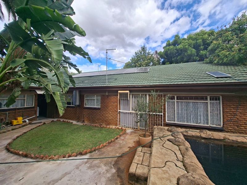 Rear exterior view of the house featuring a brick facade, tiled roof with solar panels, and a swimming pool area with adjacent garden space.