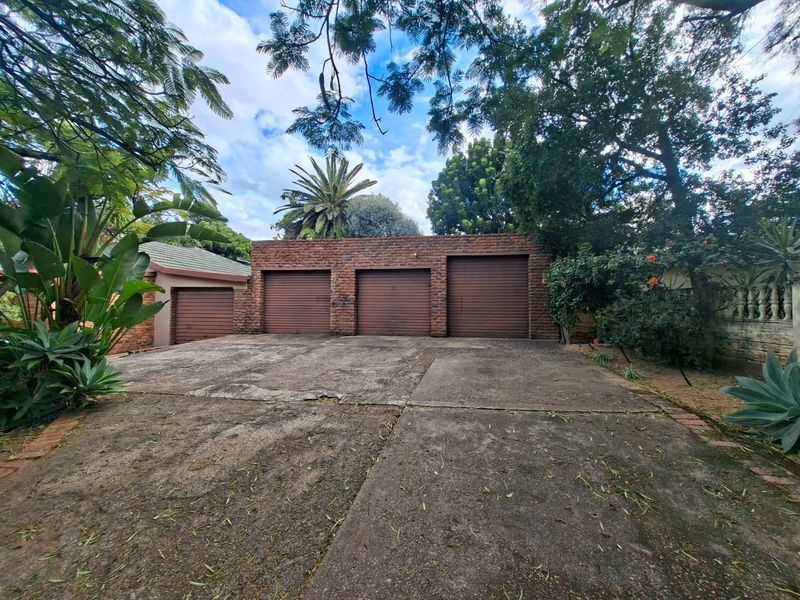 A triple garage with roller doors and a spacious concrete driveway, surrounded by mature trees and established garden landscaping.