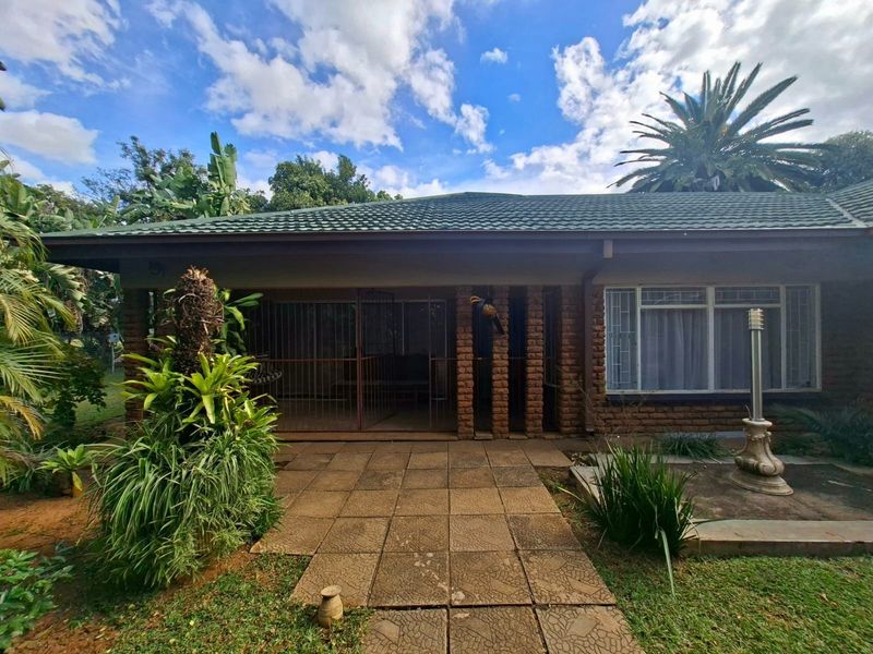 Rear view of the house featuring a paved patio area, brick facade, security gates, and a surrounding garden.