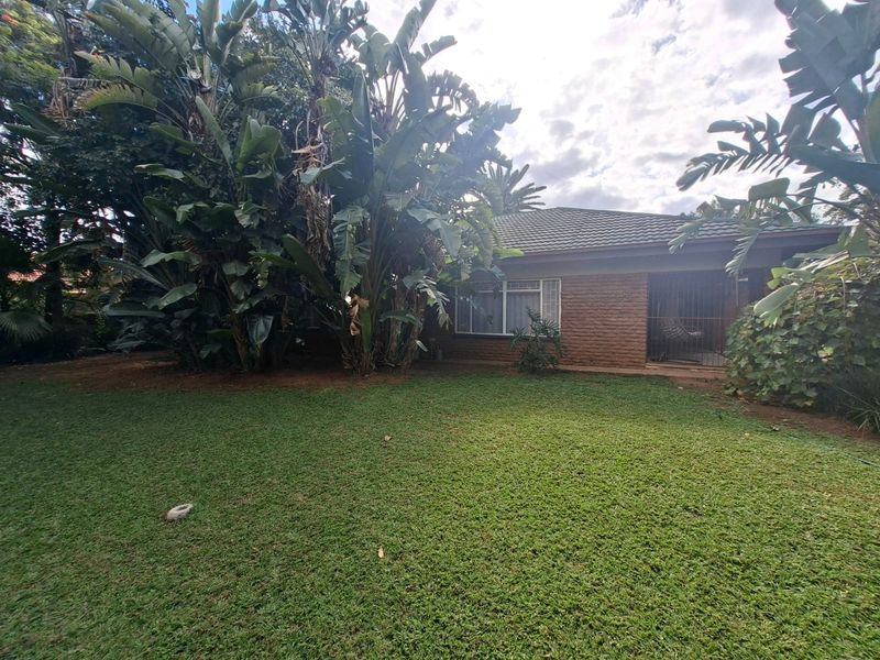 A view of the rear brick facade of the house, featuring a well-maintained lawn and established garden greenery.