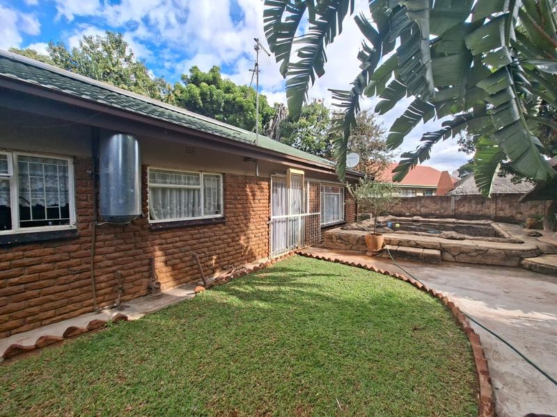 Rear exterior view featuring a brick facade, lawn area, and a rock-clad swimming pool.