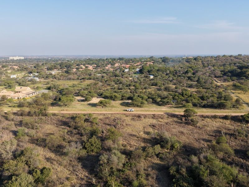 An aerial view of a large, undeveloped residential plot featuring natural vegetation, a dirt access road, and surrounding rural landscape.