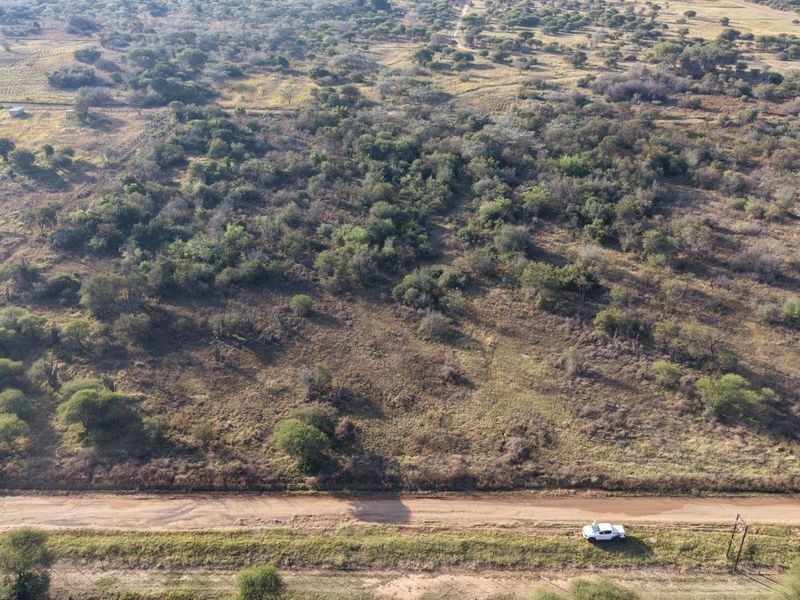 An aerial view of a large, undeveloped residential land plot featuring native vegetation and direct access to a dirt road.