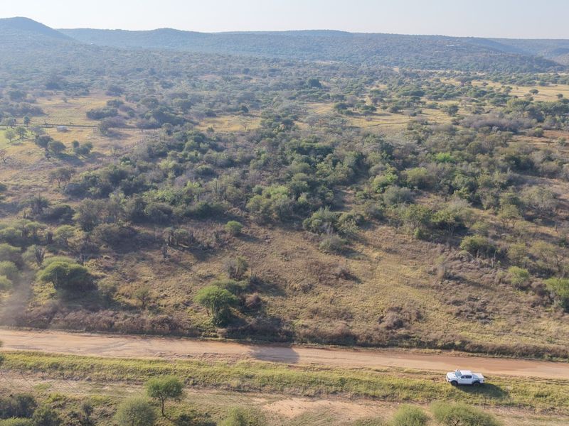 An aerial view of a large, undeveloped residential plot featuring native bushveld vegetation and access via a dirt road.