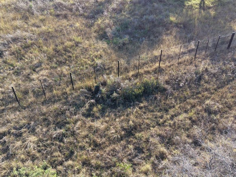 Aerial view of a vacant residential plot featuring natural grassland and existing wire perimeter fencing.