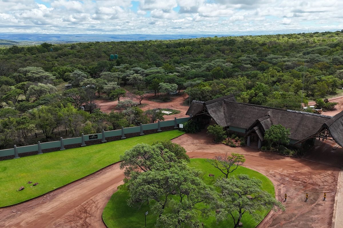 Aerial view of a residential property entrance featuring a thatched roof structure, perimeter wall, and expansive landscaped grounds set within a natural bushveld environment.
