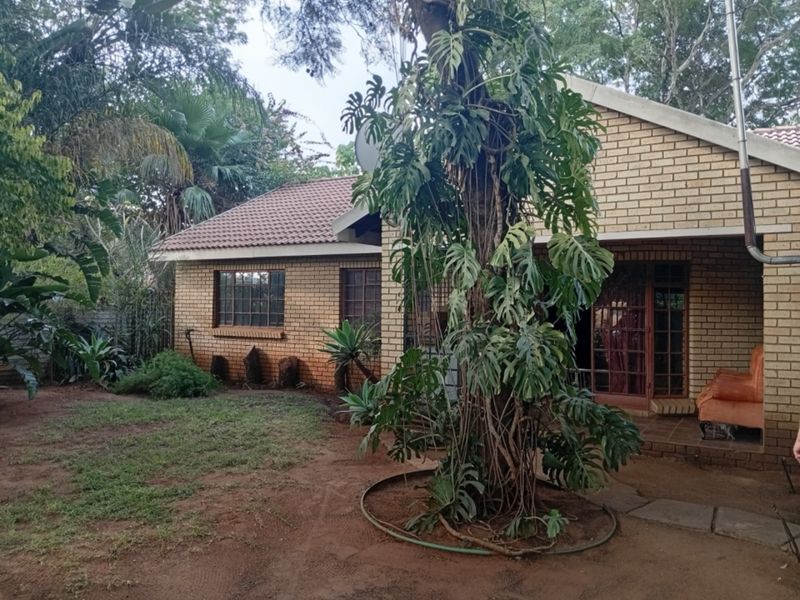 Rear view of a face brick house featuring a covered patio, tiled roof, and established garden surroundings.