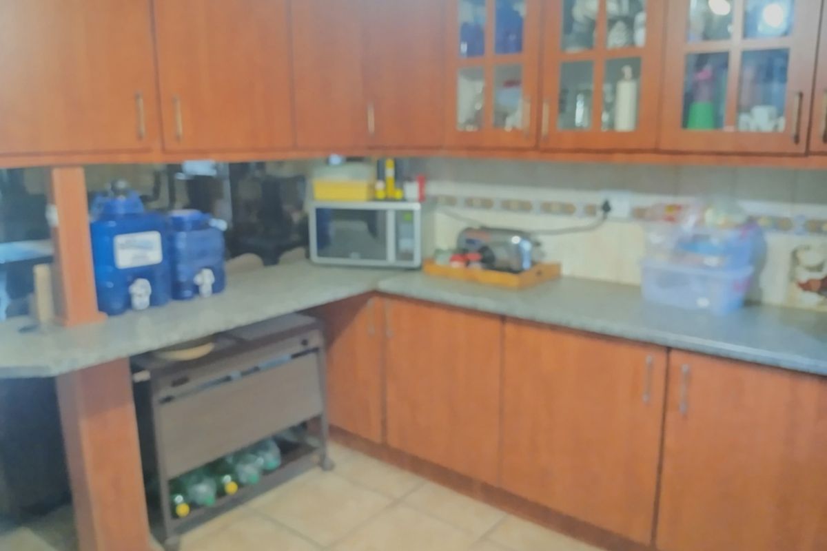 A kitchen featuring wood-look laminate cabinetry, tiled flooring, and a tiled backsplash, offering a functional layout with ample storage space.