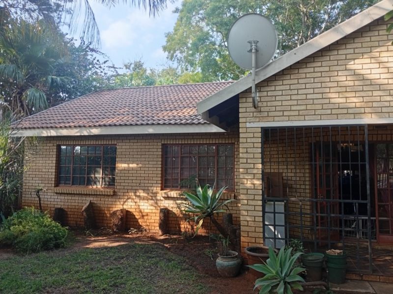 Rear view of a face brick house featuring a tiled roof, security gate, and established garden surroundings.