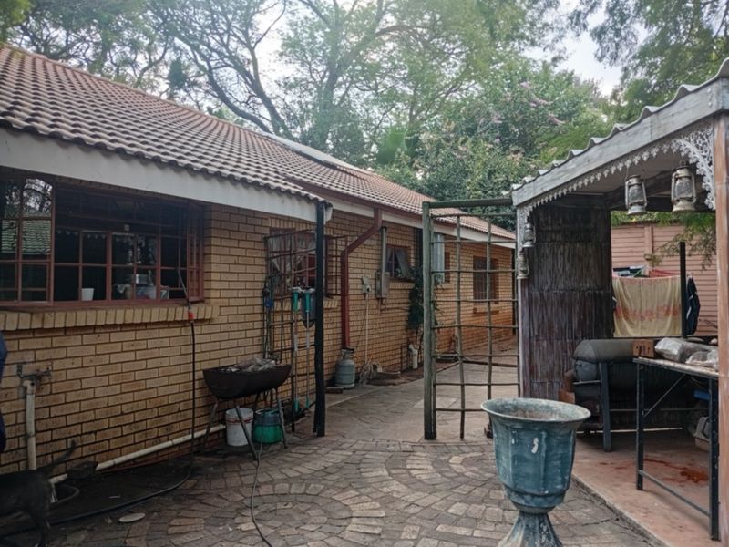 Rear exterior view of the property featuring a brick facade, tiled roof, and a paved courtyard area with a covered patio structure.