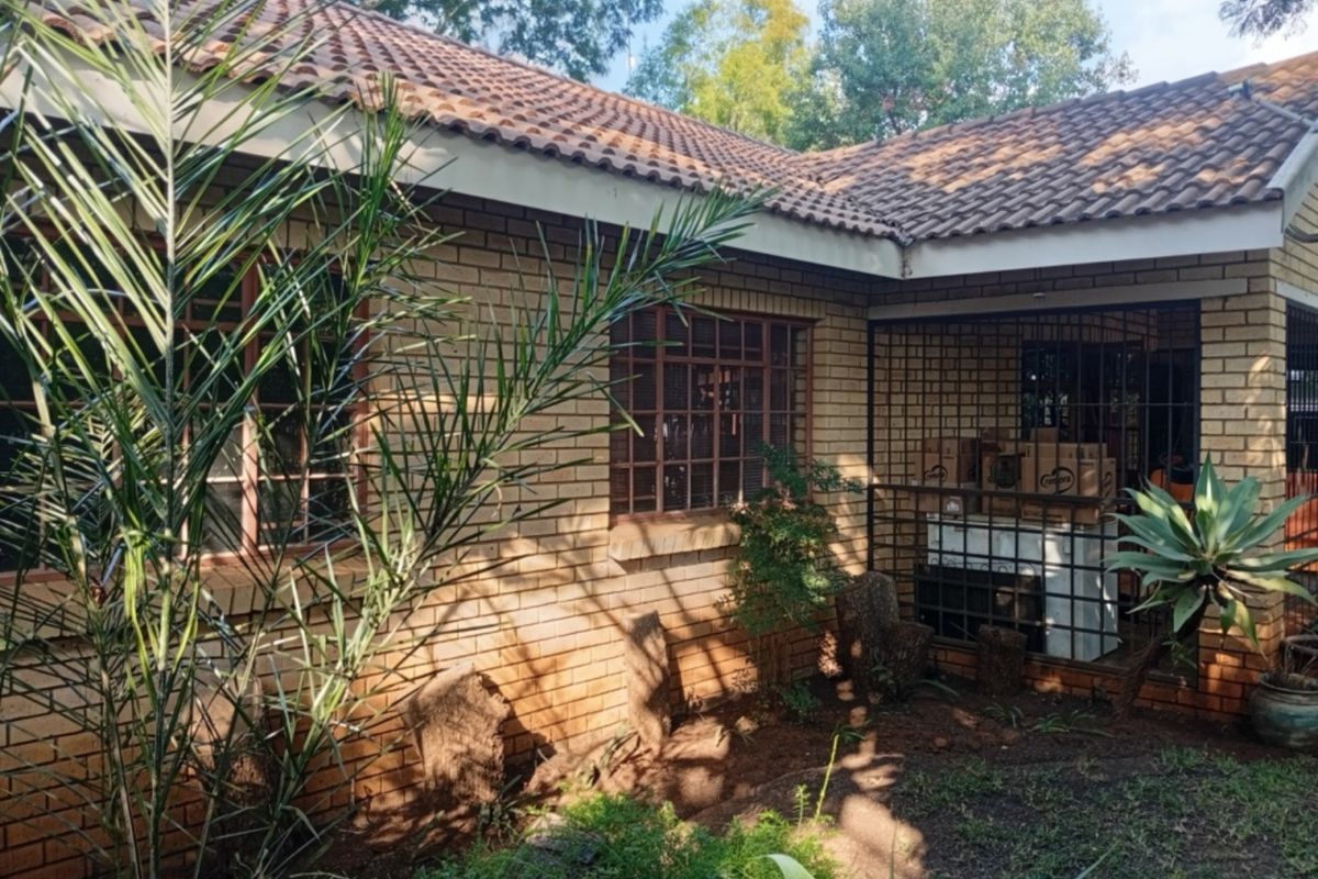 Rear exterior view of a face brick house featuring a tiled roof and security bars on the windows, set within a garden area.