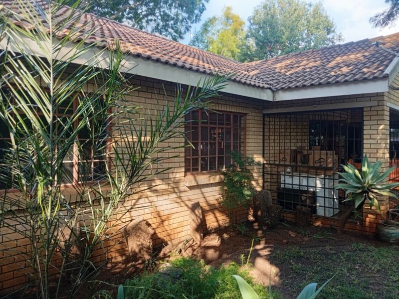 Rear exterior view of a face brick house featuring a tiled roof and security bars on the windows, set within a garden area.