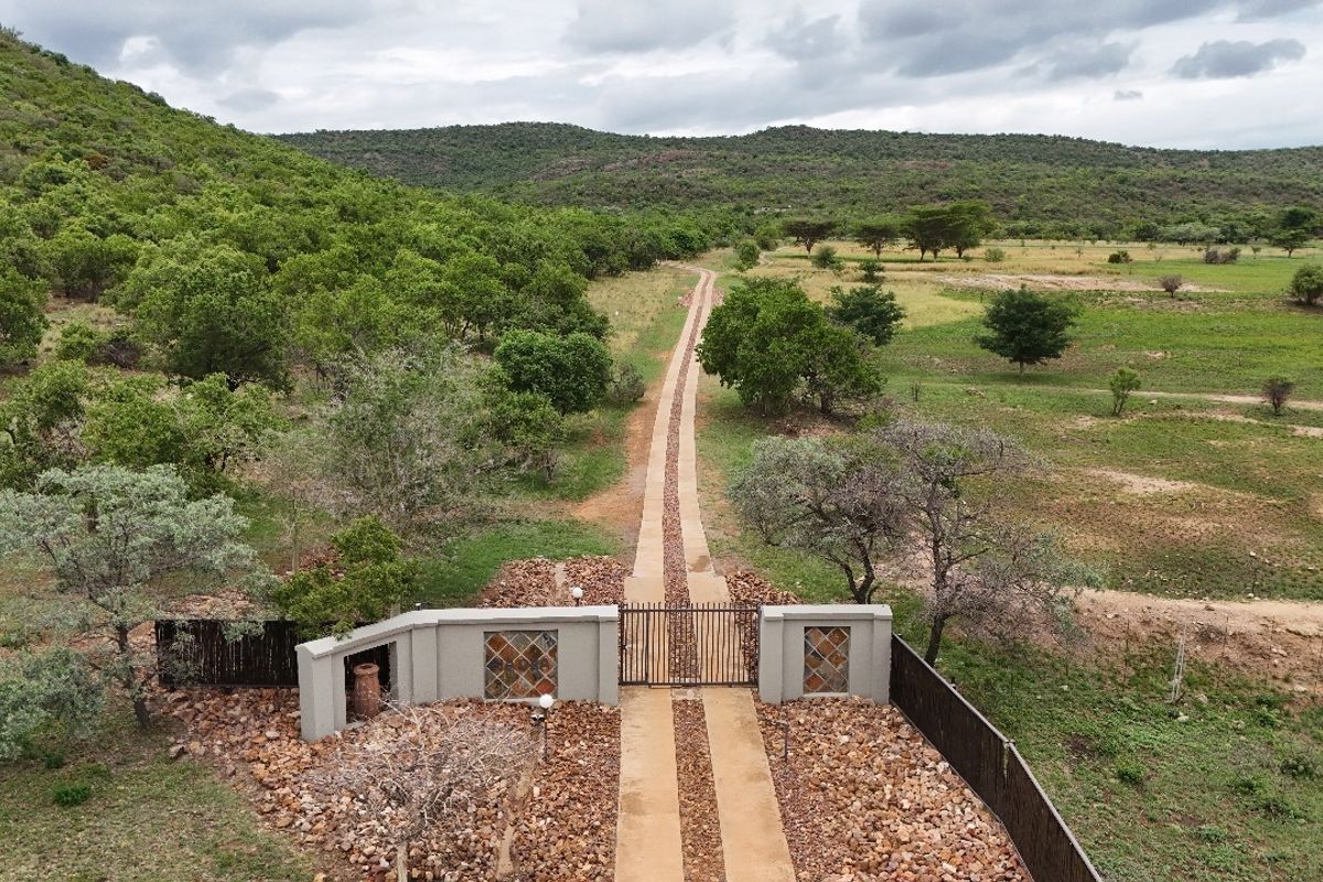 Aerial view of a residential property entrance featuring a gated driveway, perimeter fencing, and expansive surrounding natural landscape.