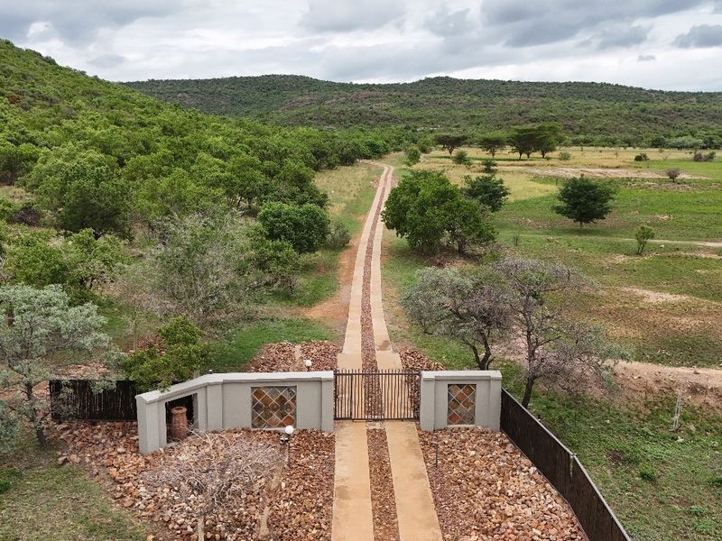 Aerial view of a residential property entrance featuring a gated driveway, perimeter fencing, and expansive surrounding natural landscape.