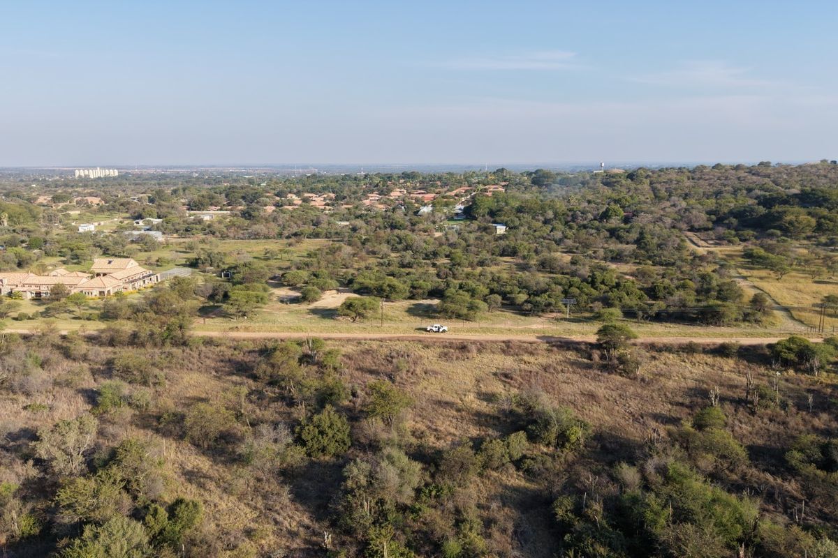 An aerial view of a large, undeveloped residential plot featuring natural vegetation, a dirt access road, and surrounding rural landscape.