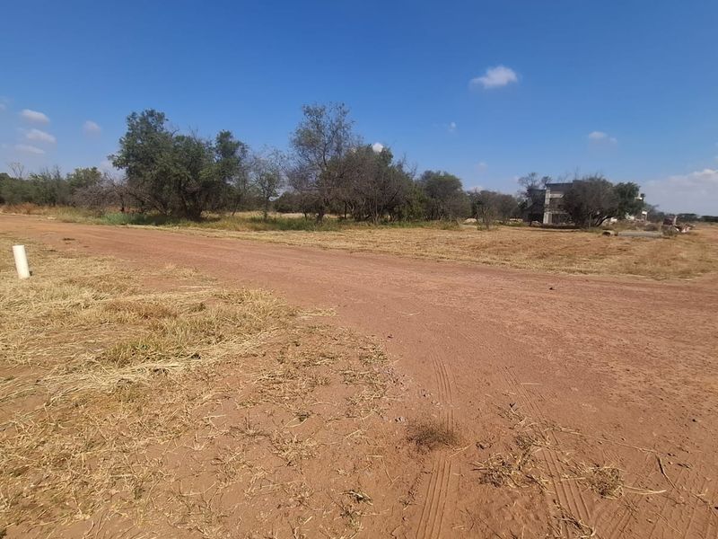 A view of a vacant residential plot featuring an unpaved access road and natural vegetation, suitable for future development.