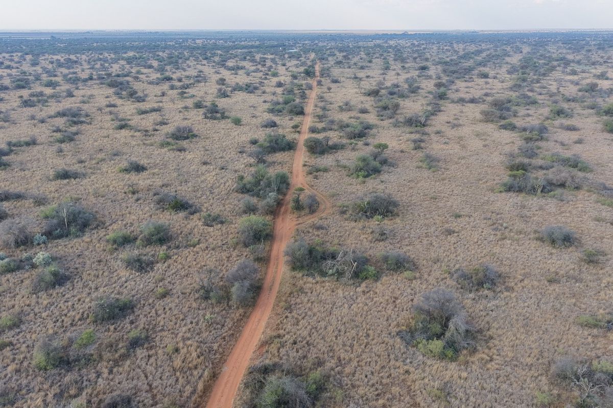 An aerial view of the expansive farm landscape featuring a central dirt access road winding through natural bushveld vegetation.