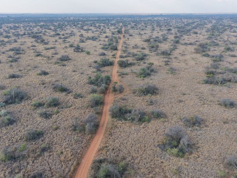 An aerial view of the expansive farm landscape featuring a central dirt access road winding through natural bushveld vegetation.
