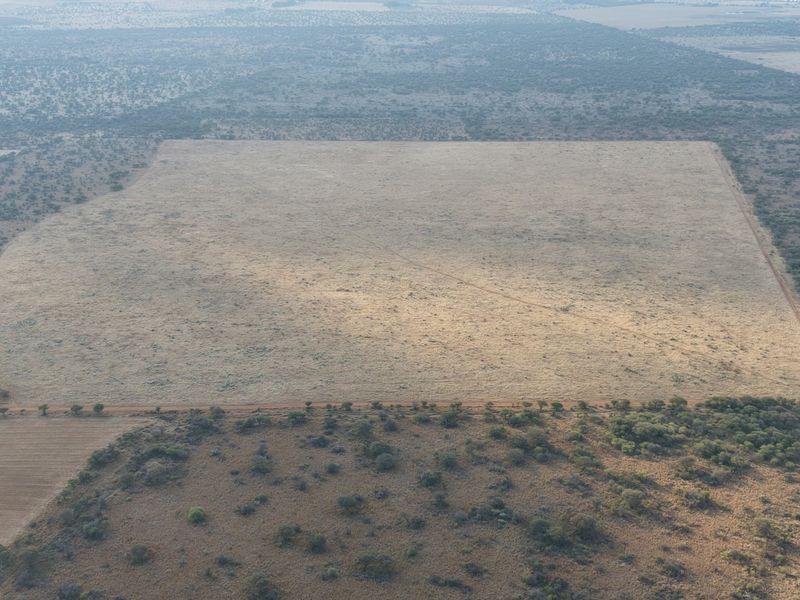 An aerial view of a large, open agricultural field surrounded by natural bushveld and scrubland, featuring clear boundary lines and access tracks.