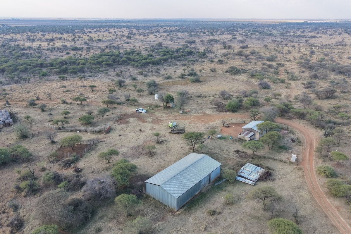 Aerial view of a rural farm property featuring a large metal shed, outbuildings, water storage, and extensive surrounding bushveld landscape.