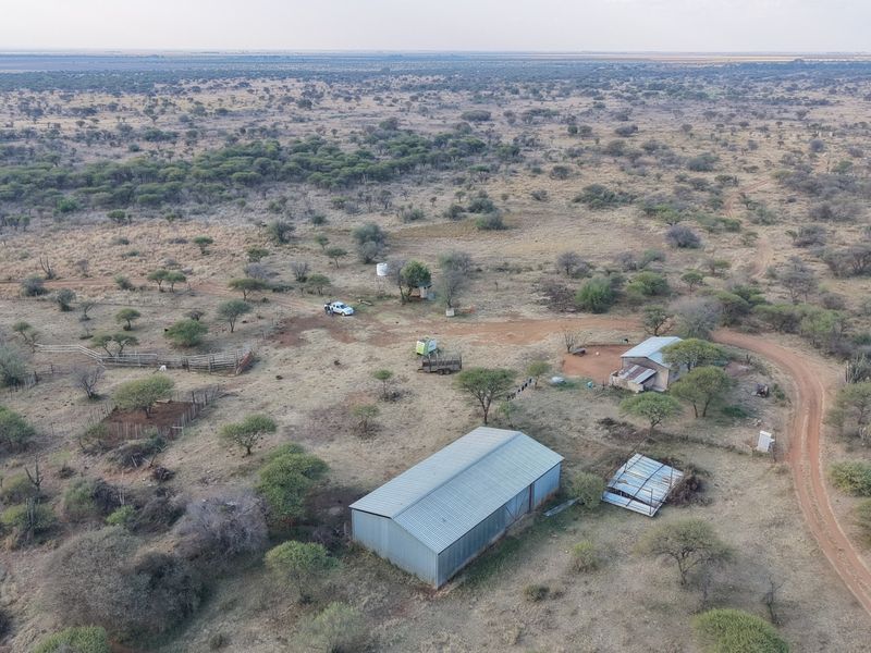 Aerial view of a rural farm property featuring a large metal shed, outbuildings, water storage, and extensive surrounding bushveld landscape.
