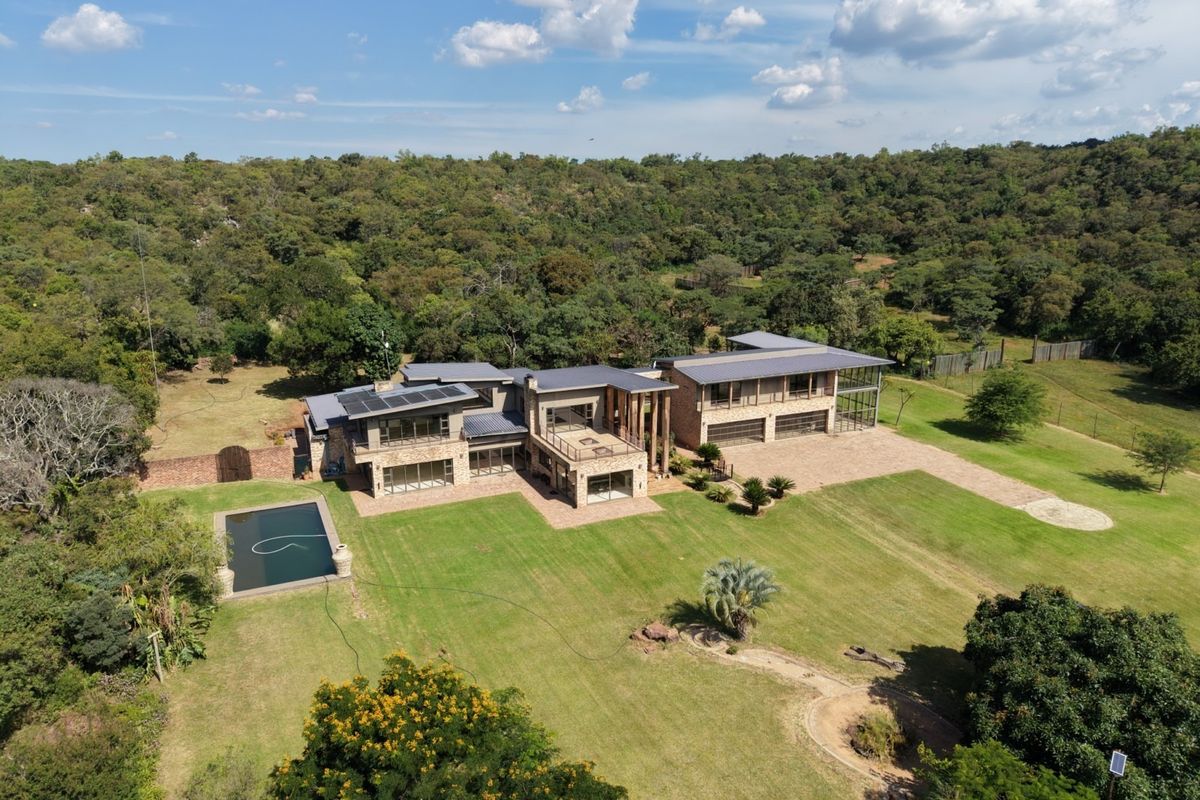 Aerial view of a large modern farm estate featuring stone-clad architecture, a swimming pool, solar panels, and expansive landscaped grounds.