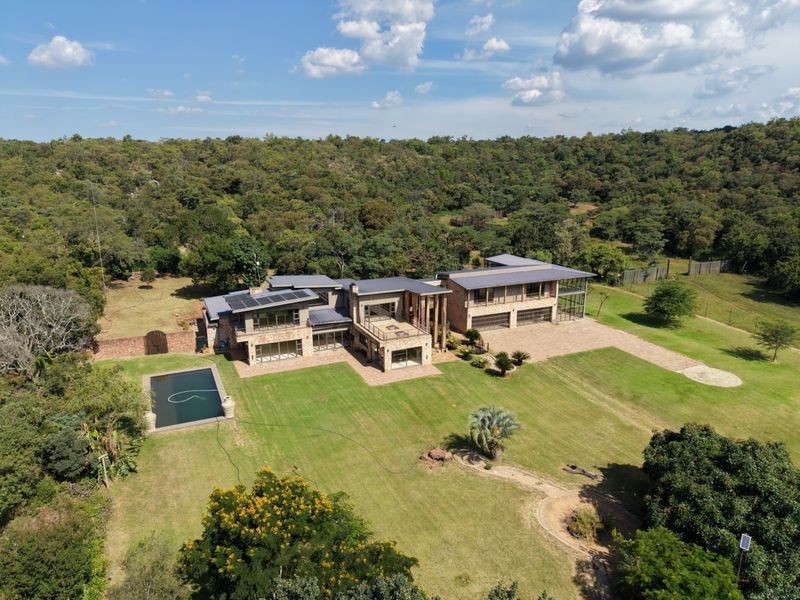 Aerial view of a large modern farm estate featuring stone-clad architecture, a swimming pool, solar panels, and expansive landscaped grounds.