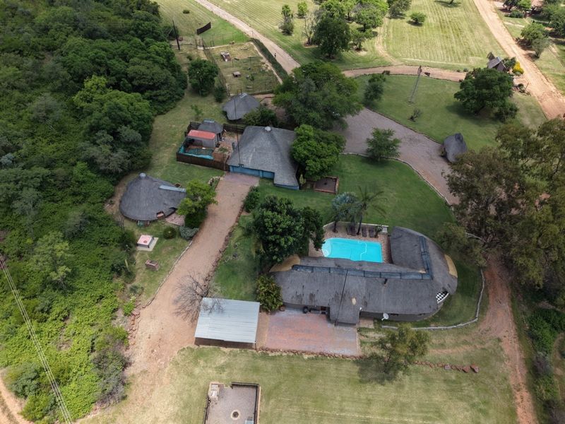Aerial view of a farm property featuring multiple thatched-roof structures, a swimming pool, a carport, and expansive landscaped grounds.