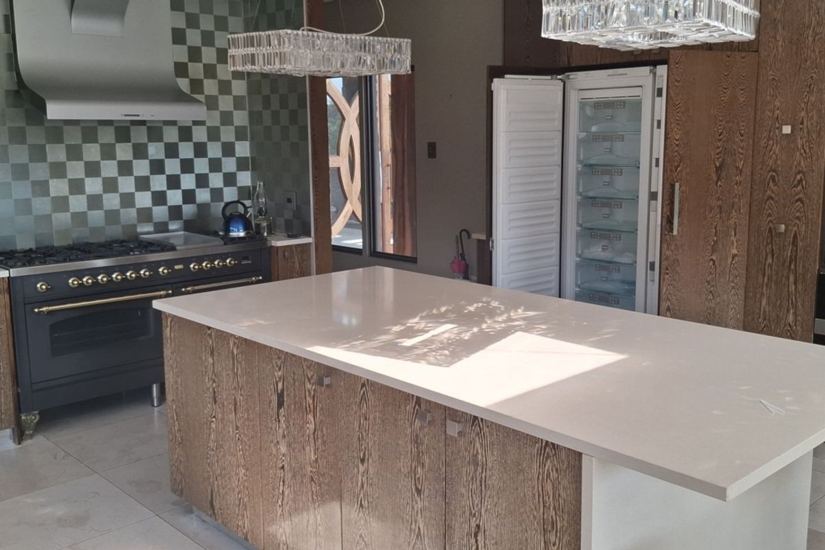 Modern kitchen featuring a large central island, high-end integrated appliances, wooden cabinetry, and a stylish tiled backsplash.