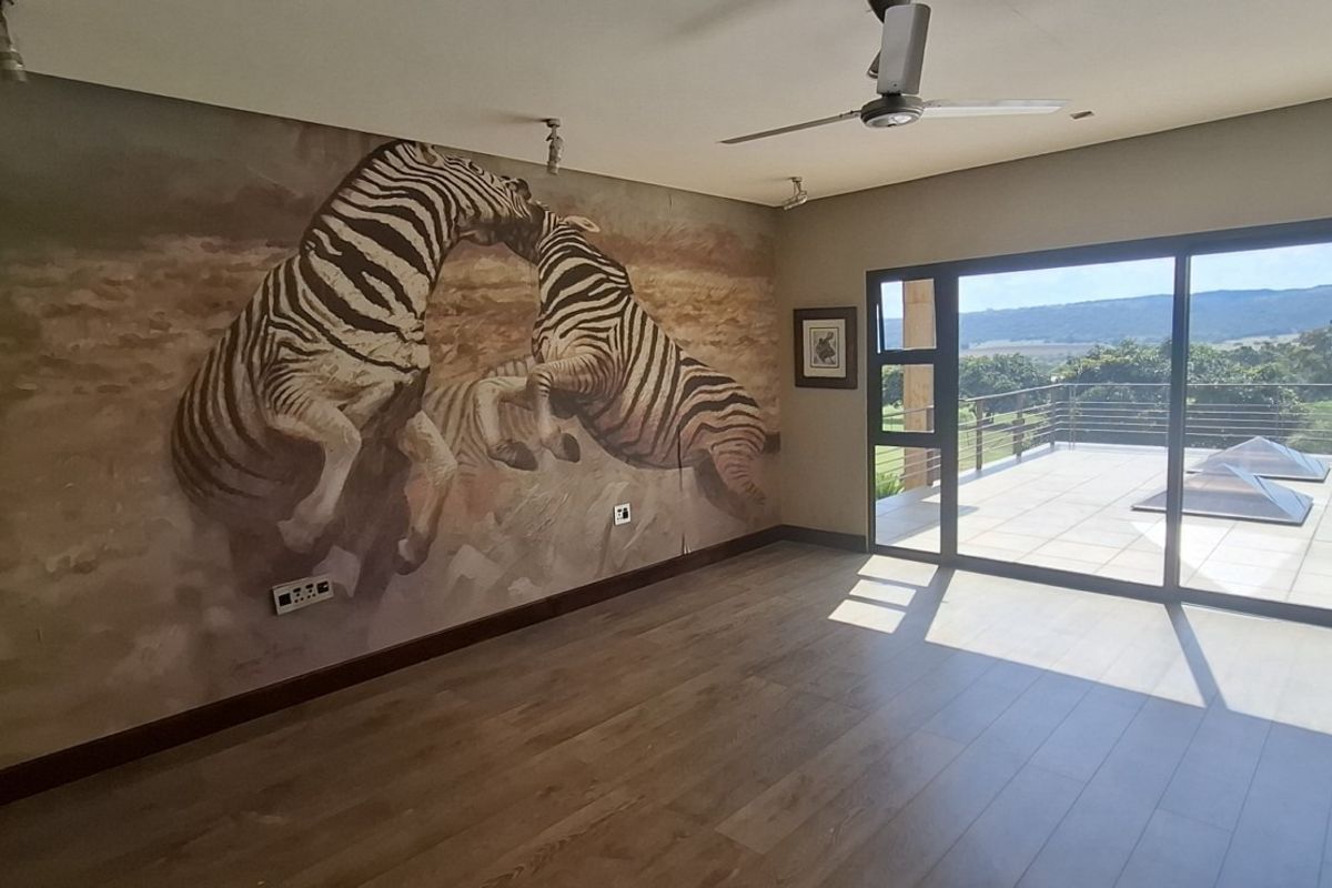 Spacious living area featuring large sliding glass doors opening to a balcony, laminate flooring, ceiling fan, and a decorative mural wall.