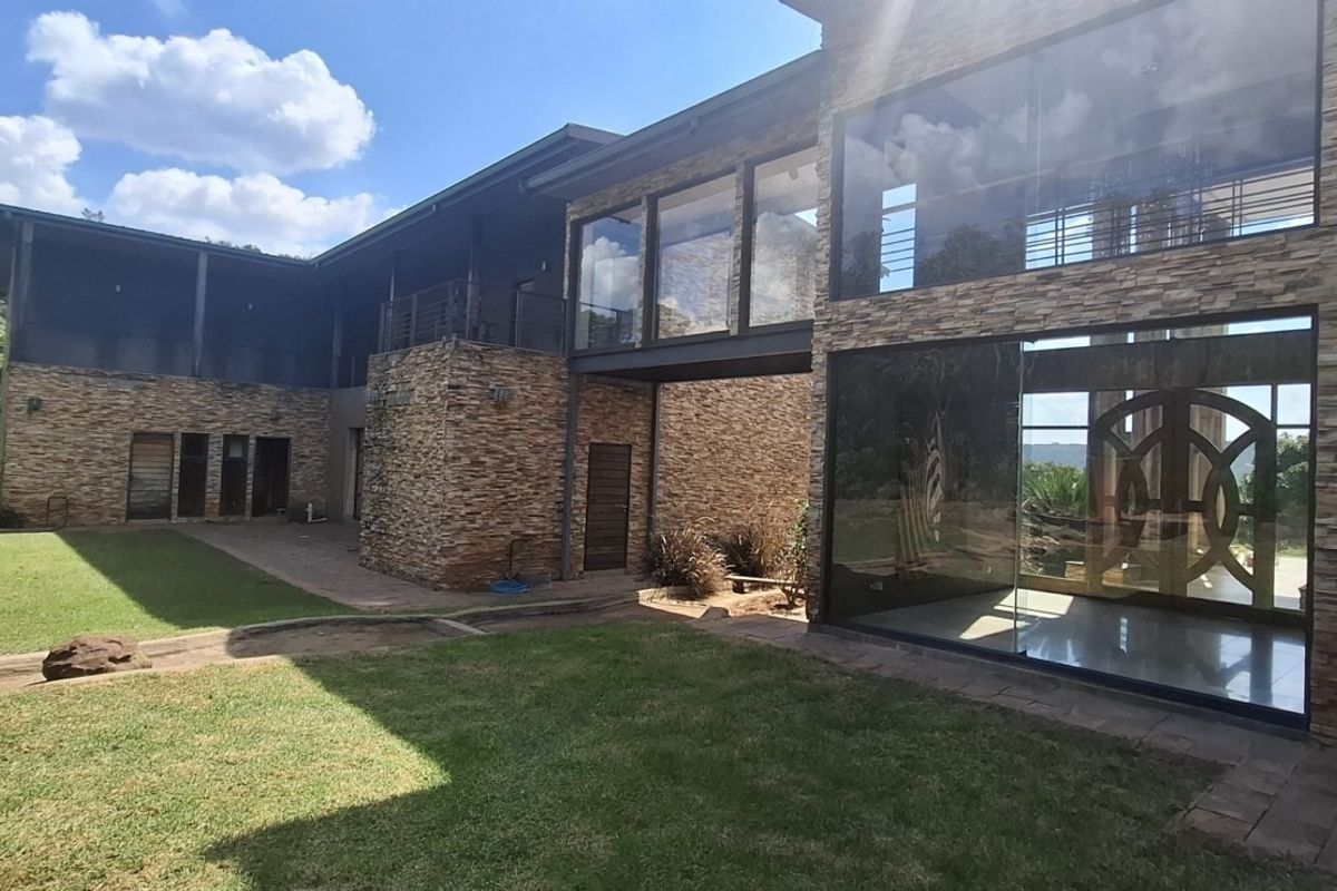 Modern multi-level farmhouse exterior featuring extensive stone cladding, large glass windows, and a covered patio area overlooking a landscaped garden.