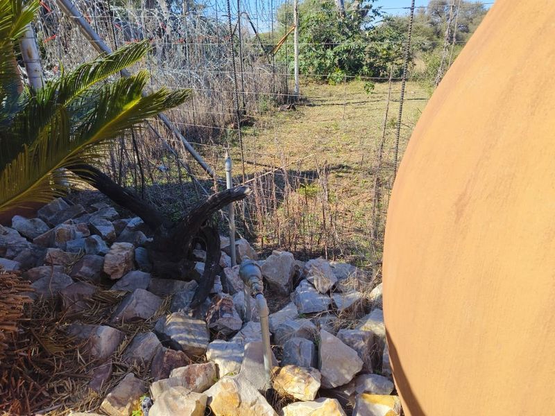 A view of the property boundary featuring wire mesh fencing, a water meter, and rock landscaping in a natural garden setting.