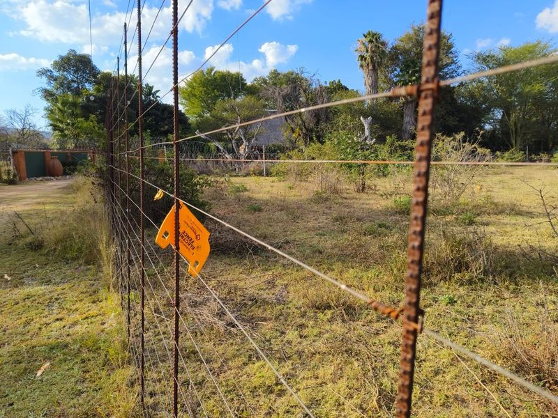 A view of the vacant residential land featuring perimeter wire mesh fencing with electric fence warning signage.