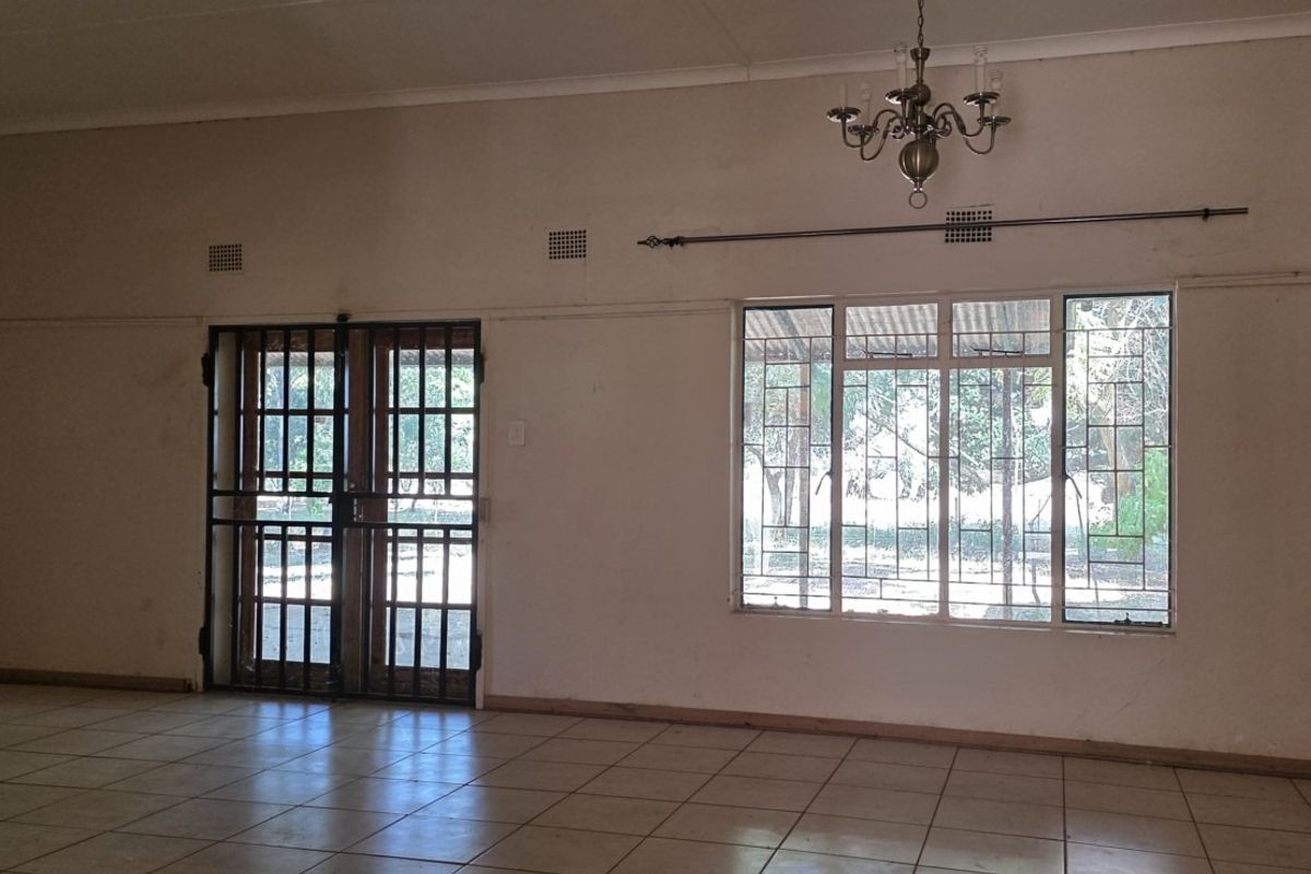 Spacious, empty living area featuring tiled flooring, security gates, and metal-framed windows with security bars, offering a blank canvas for renovation.