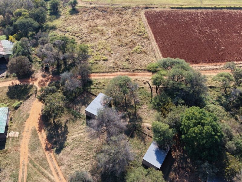 Aerial view of a farm property featuring multiple outbuildings with metal roofs, dirt access tracks, and surrounding agricultural land.