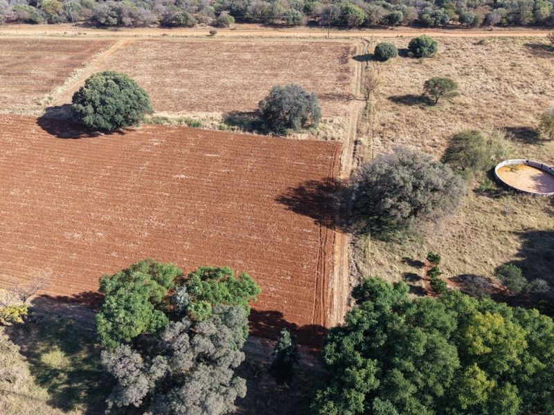 Aerial view of the farm property featuring expansive cultivated fields, mature trees, and a circular water reservoir.