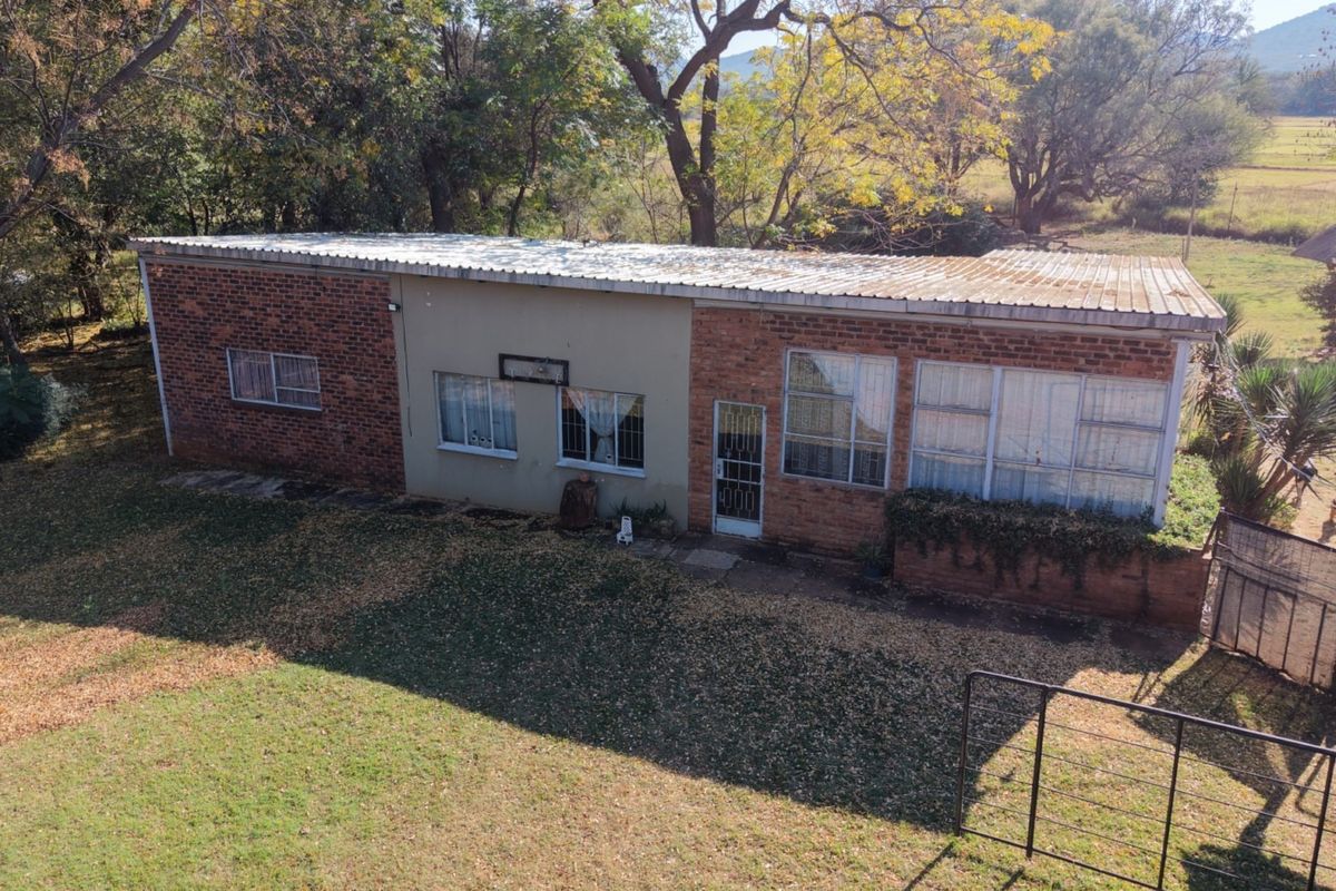Aerial view of a single-story brick farmhouse featuring a corrugated metal roof and large windows, set within a rural landscape.